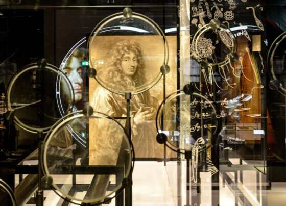 A collection of lens set up in front of a drawn portrait of Christiaan Huygens.