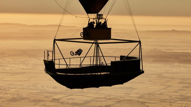 BMX rider performs tricks on platform suspended from hot air balloon