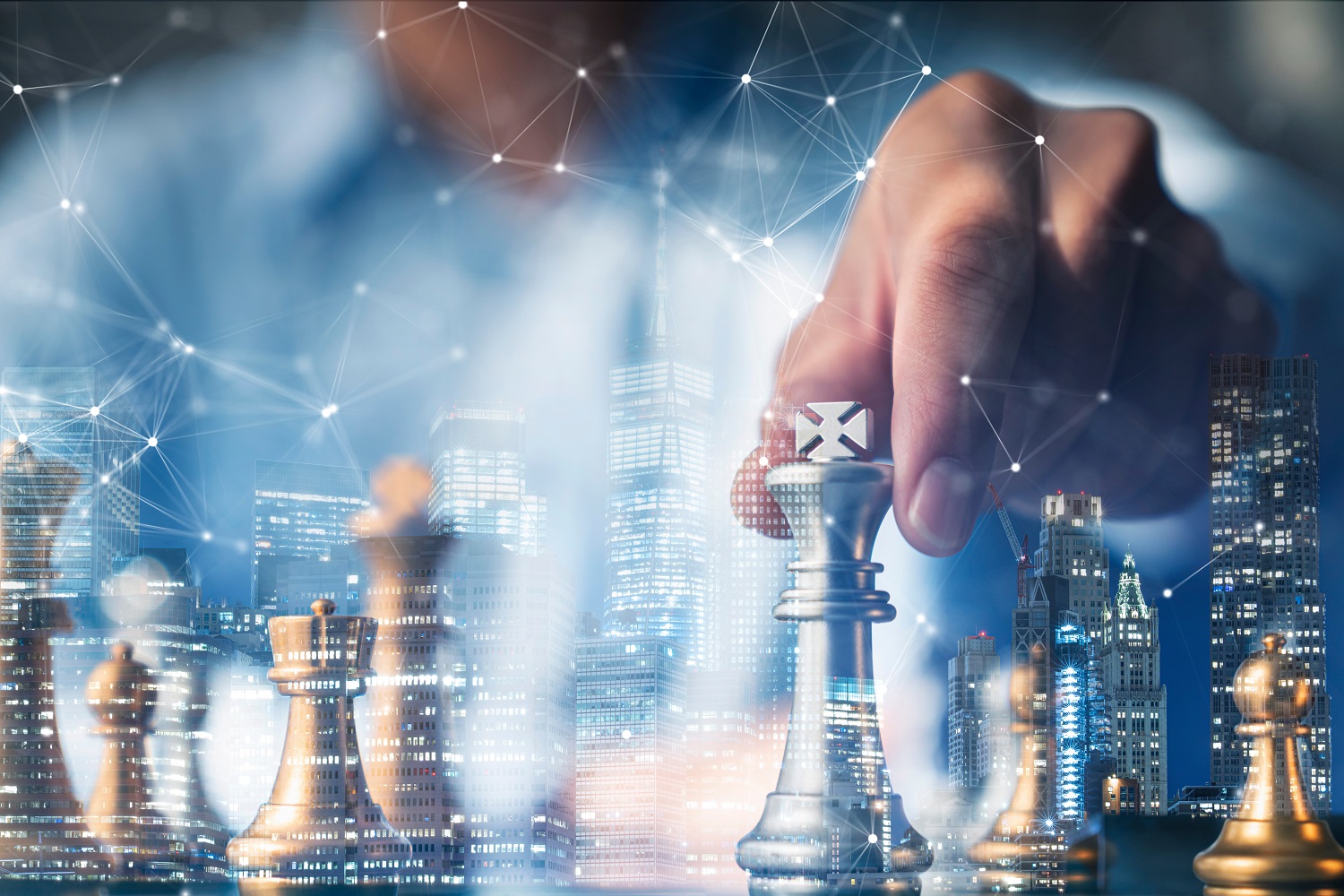 A person’s hand moves a king chess piece, against a backdrop of other chess pieces and tall city buildings.