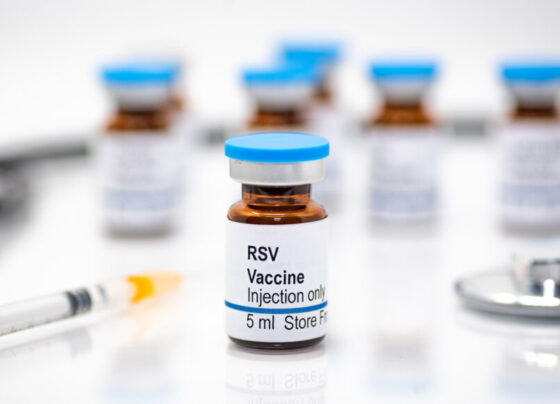 A photo of an RSV vaccine bottle with a syringe, stethoscope and other vaccine bottle on a white background.