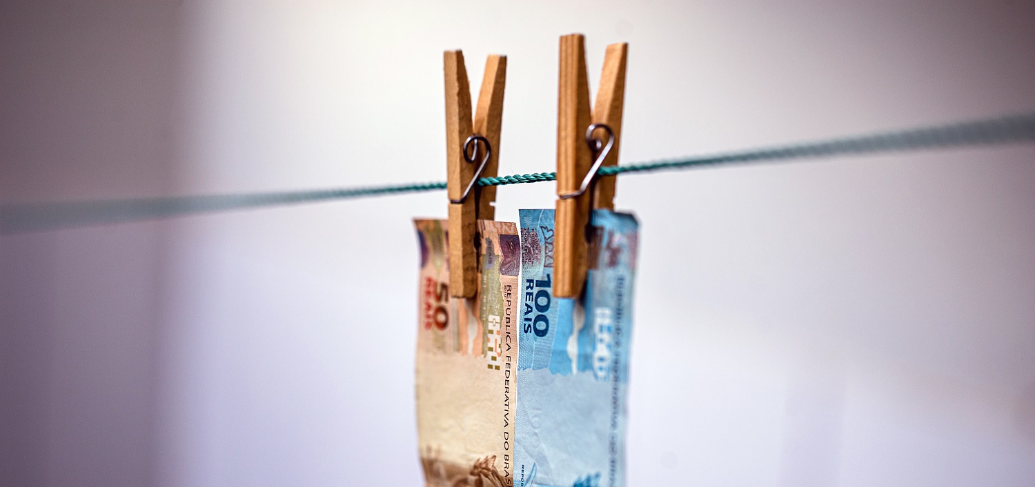 Two Brazilian real banknotes on a laundry line, attached with clothes pegs.