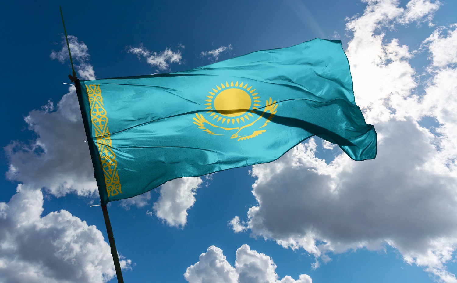 The flag of Kazakhstan mounted on a pole, fluttering in the wind.