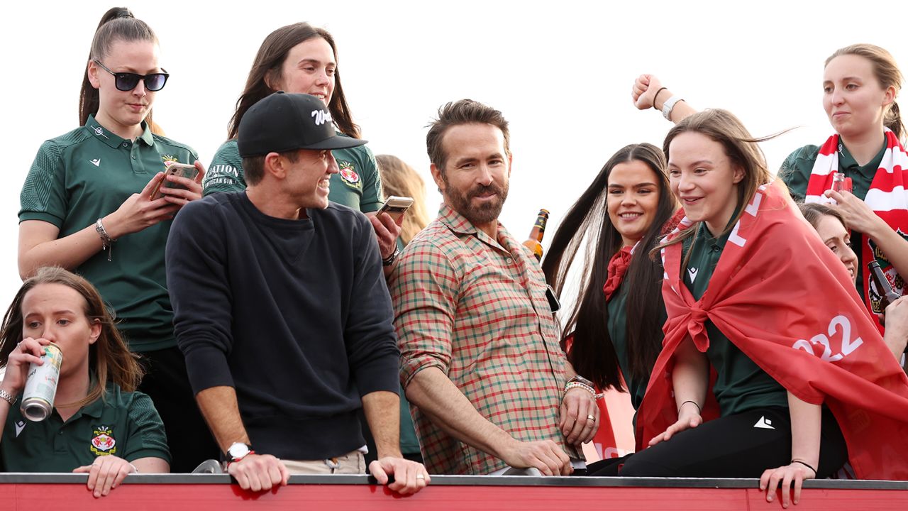 Rob McElhenney, Co-Owner of Wrexham, and Ryan Reynolds, Co-Owner of Wrexham, look on as they celebrate with players of Wrexham Women during a Wrexham FC Bus Parade following their Title Winning Season in the Genero Adran North on May 2, 2023 in Wrexham, Wales.