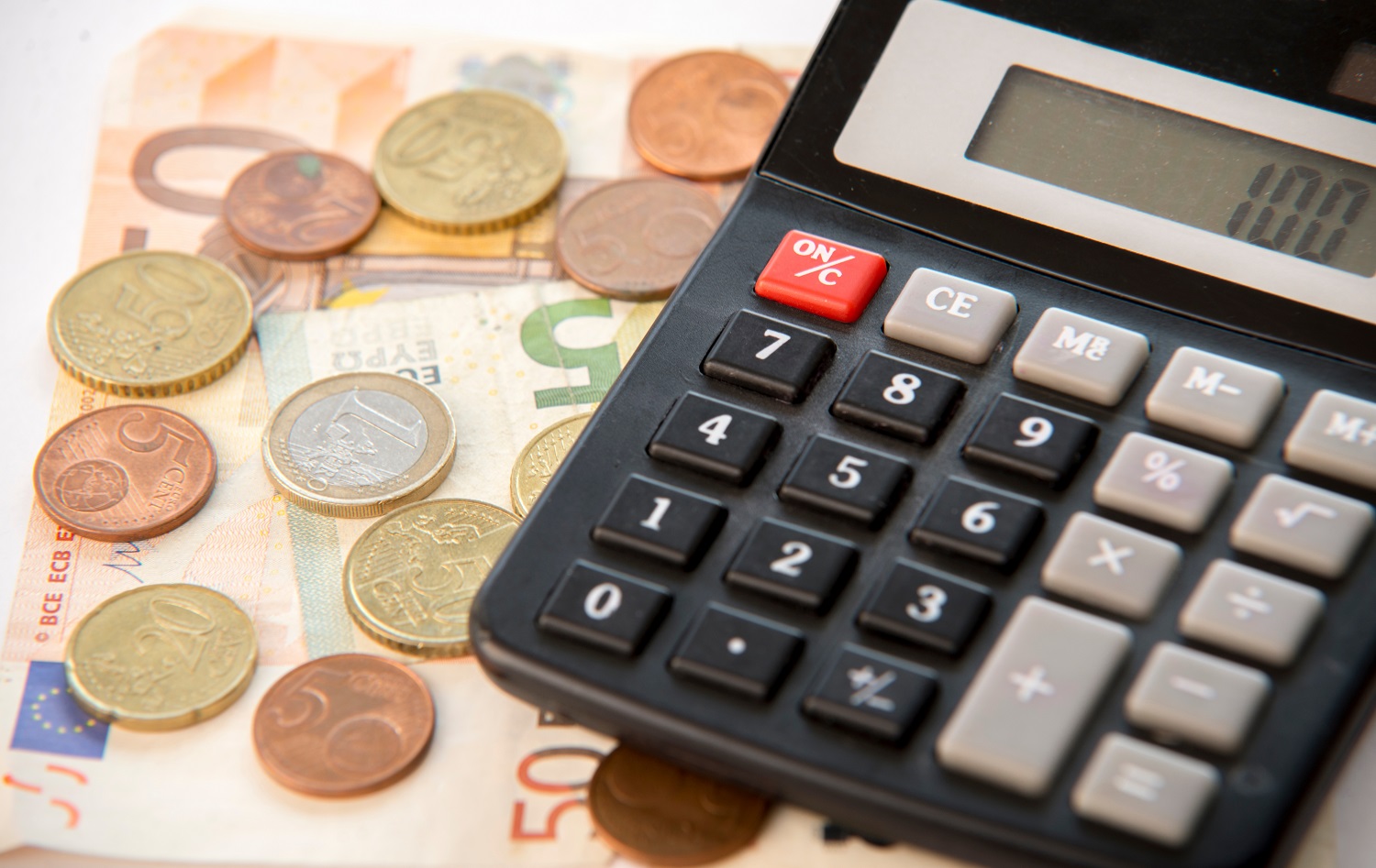 A calculator rests on a pile of euro banknotes and beside coins of the same currency.