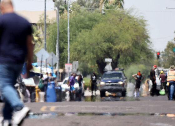 A photo of a busy street with people walking around and cars on the road. Heat haze can be seen on the road.