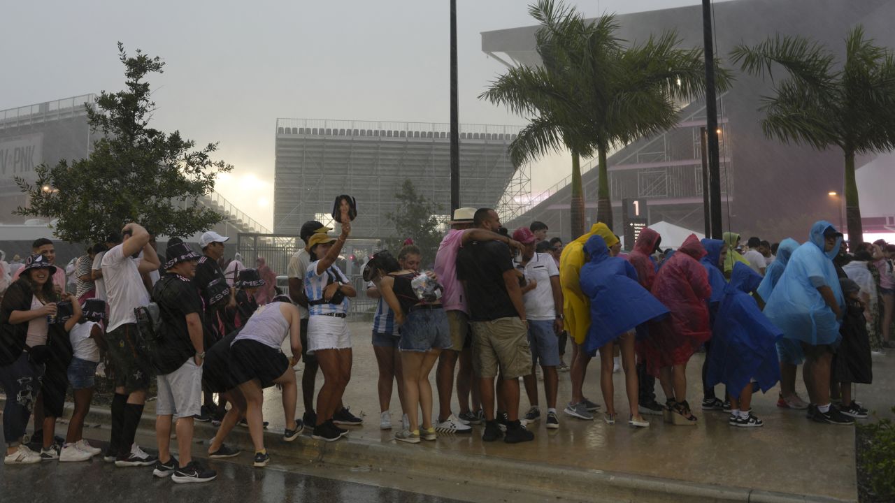 Fans wait in line in a downpour to enter DRV PNK Stadium, home of the Inter Miami MLS soccer team, for an event to present international superstar Lionel Messi one day after the team finalized his signing through the 2025 season, Sunday, July 16, 2023, in Fort Lauderdale, Fla. (AP Photo/Rebecca Blackwell)