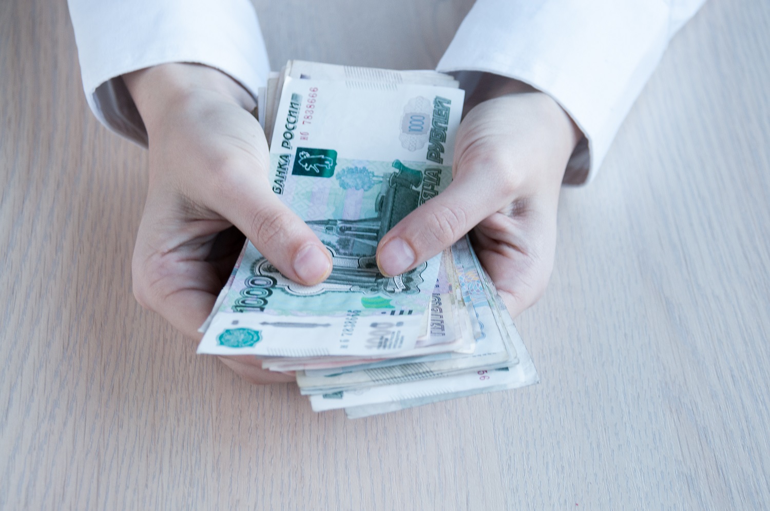 A person seated at a desk holds Russian banknotes in their hand.