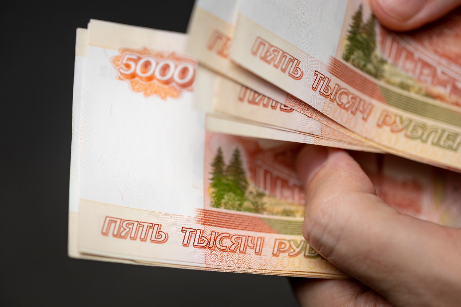 A person holds a handful of Russian 5,000 ruble banknotes in two hands.