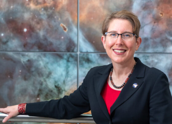 A photo of Jane Rigby standing in front of a large galaxy image.