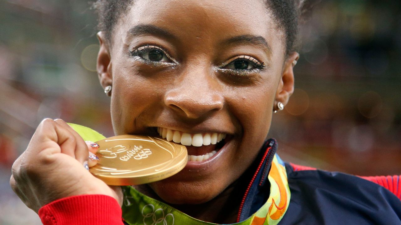 FILE - United States' Simone Biles bites her gold medal for the artistic gymnastics women's individual all-around final at the 2016 Summer Olympics in Rio de Janeiro, Brazil, Aug. 11, 2016. (AP Photo/Dmitri Lovetsky, File)