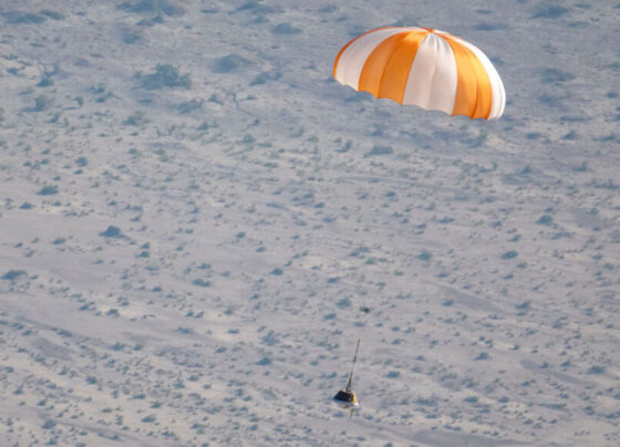 A photo of a small space capsule parachuting down to land in Utah.