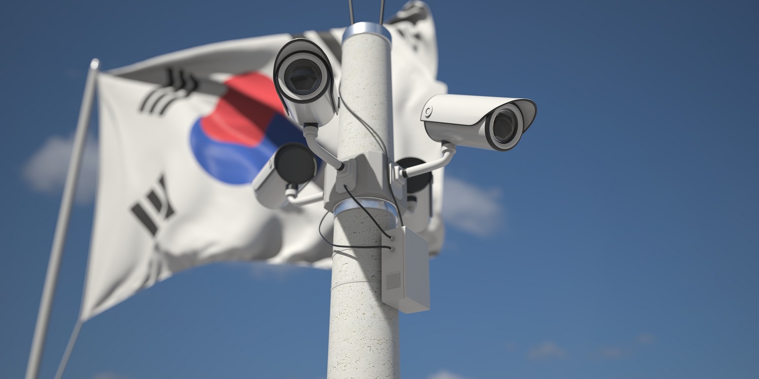 A nest of outdoor CCTV security cameras near the flag of South Korea, mounted on a flagpole.