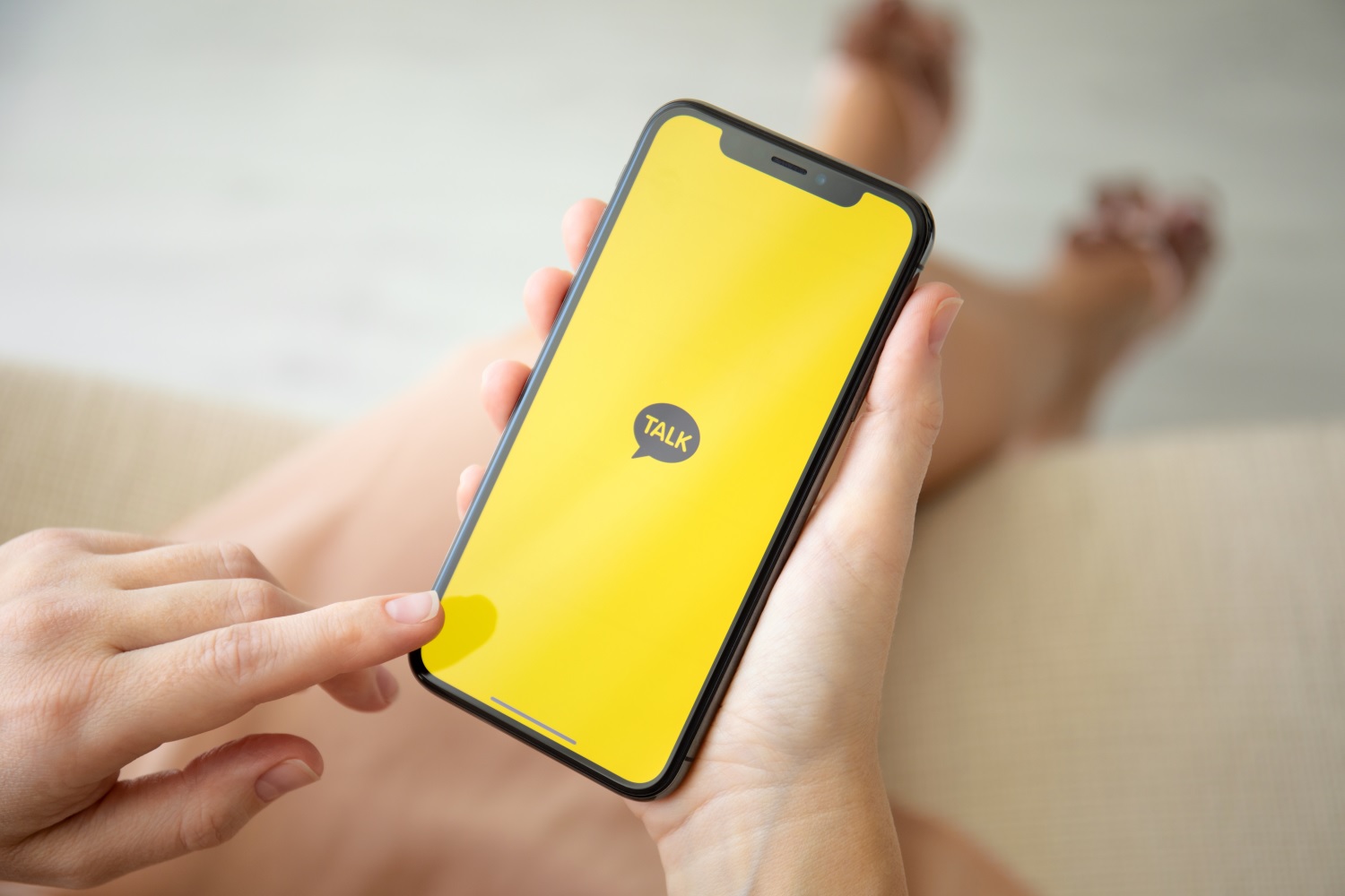 A woman holds an iPhone running the KakaoTalk app.