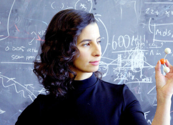 Quantum astrochemist Clara Sousa-Silva stands in front of a blackboard, holding a molecular model in her hand.