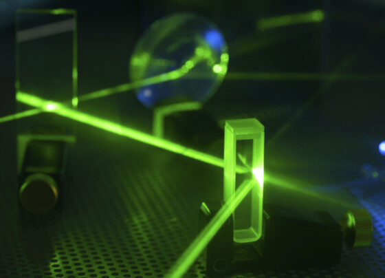 A photo of a green laser beam being sent through several pieces of glass.