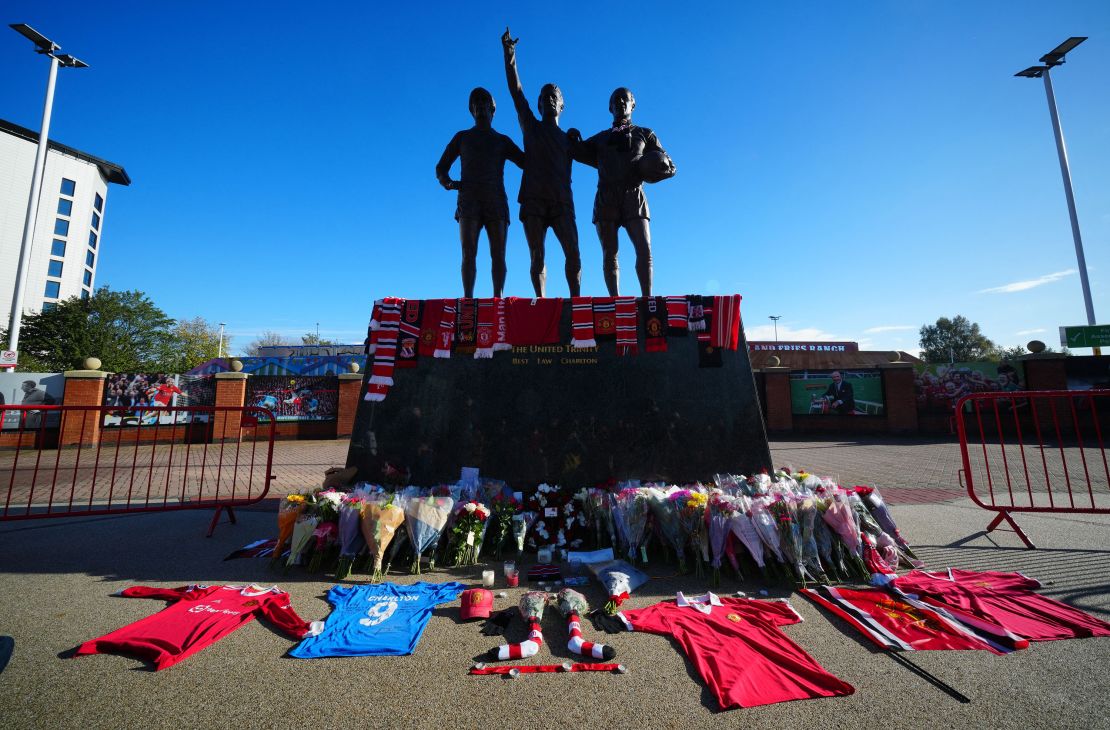 Tributes and flowers are pictured at the base of the 'United Trinity' sculpture, depicting former Manchester United players George Best, Denis Law and Bobby Charlton, following the death of Bobby Charlton, outside of Old Trafford football stadium in Manchester, central England, on October 22, 2023. England World Cup winner and Manchester United great Bobby Charlton, described by the club as a "giant of the game", has died at the age of 86, it was announced on Saturday.