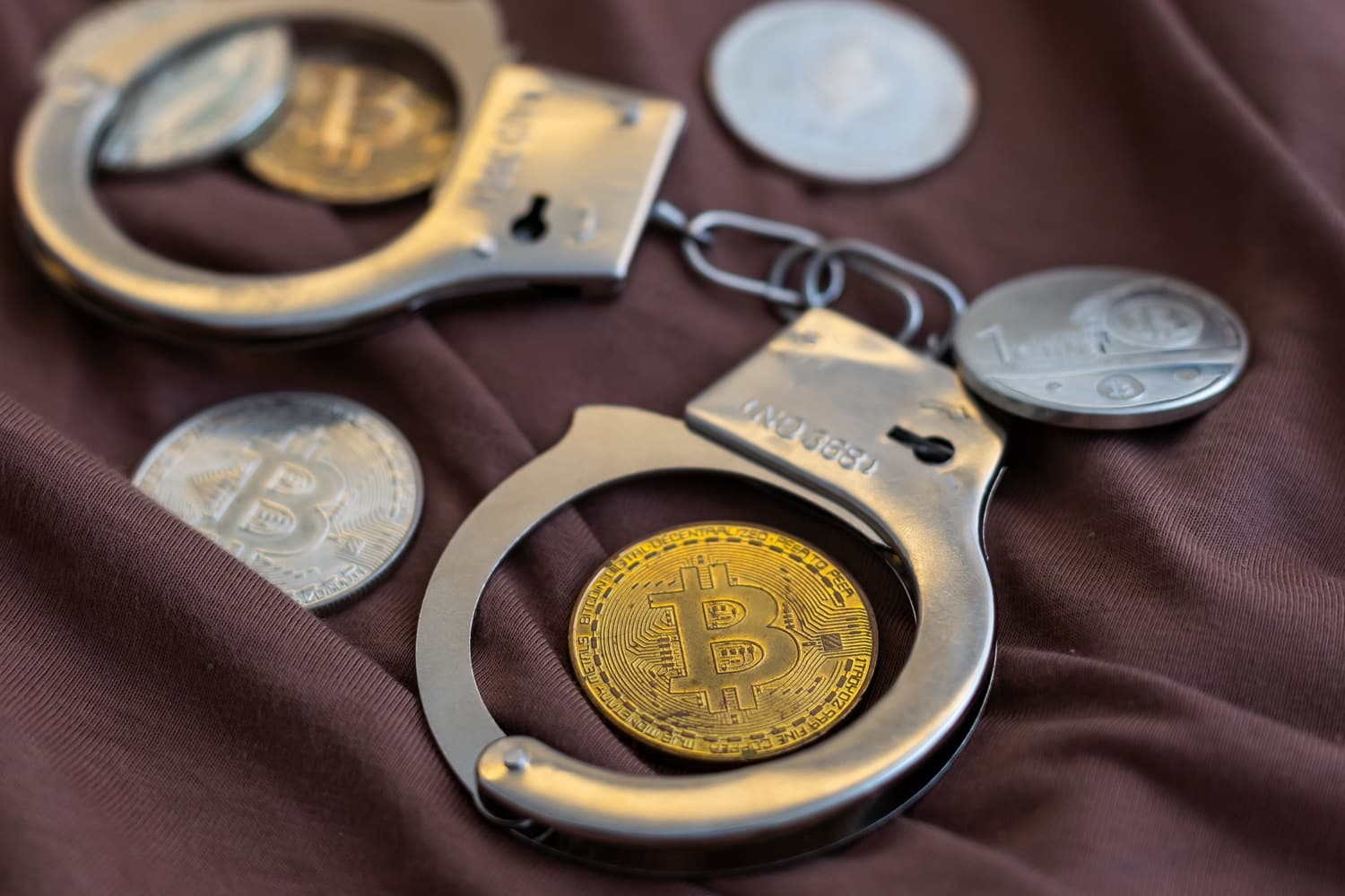 Metal coins intended to represent Bitcoin and other cryptoassets with a pair of police handcuffs.