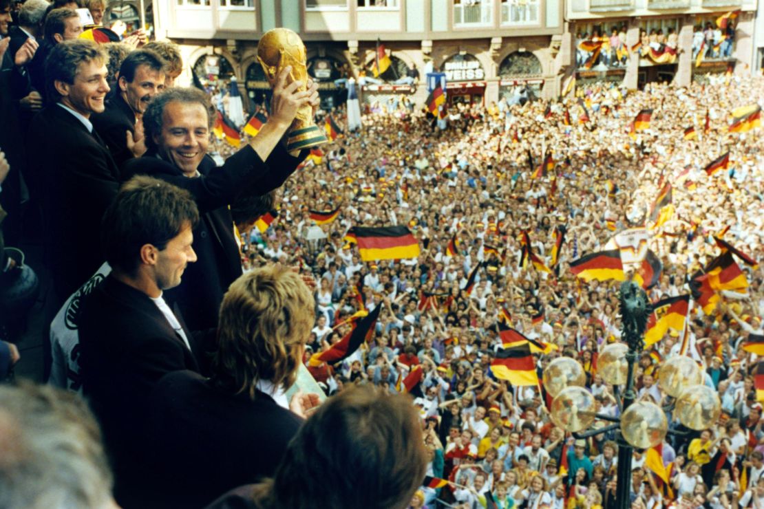 ARCHIV - Viele tausend Menschen bereiten den Spielern der deutschen Fußball-Weltmeistermannschaft am 09.07.1990 auf dem Römerberg in Frankfurt am Main einen begeisterten Empfang mit viel Jubel und einem Meer an deutschen Fahnen. Teamchef Franz Beckenbauer (mit Pokal) hält auf dem Balkon des Römers, flankiert von seinen Spielern, lachend den in Italien gewonnenen Weltmeister-Pokal in die Höhe. Die deutsche Fußball-Nationalmannschaft ist zum drittenmal nach 1954 und 1974 Weltmeister. Photo by: Kai-Uwe Wärner/picture-alliance/dpa/AP Images