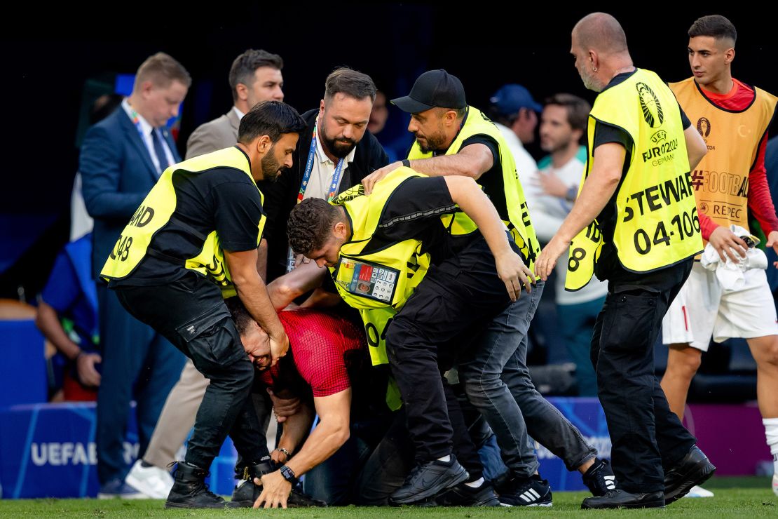 A pitch invader is carted off the pitch during the match.