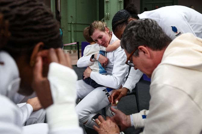 French fencer Auriane Mallo-Breton holds her son, Mathis, as her team gathers with coaches after an épée win against South Korea on July 30.