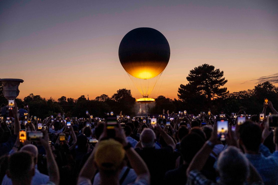 Visitors take pictures of the Olympic cauldron as it rises high after sunse on day two of the Olympic Games Paris 2024 at on July 28, 2024 in Paris, France.