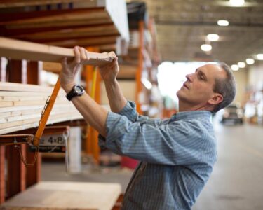 A person moving lumber off a shelf at a warehouse.