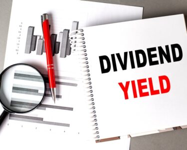 The words Dividend Yield in a notebook sitting on top of paper with a graph on it and a magnifying glass.