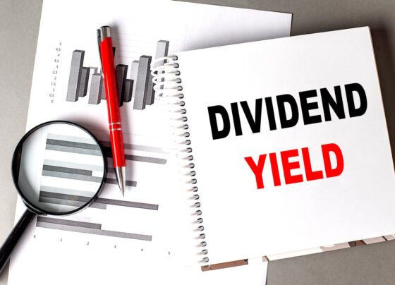 The words Dividend Yield in a notebook sitting on top of paper with a graph on it and a magnifying glass.