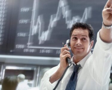 A person on the phone pointing to upward movement on a stock chart.