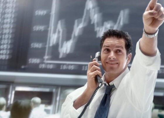 A person on the phone pointing to upward movement on a stock chart.