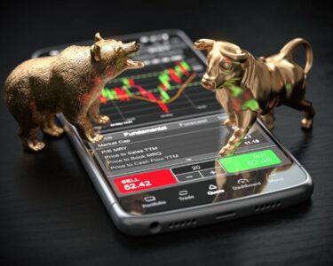 Statues of a bull and bear atop a phone with stock charts.