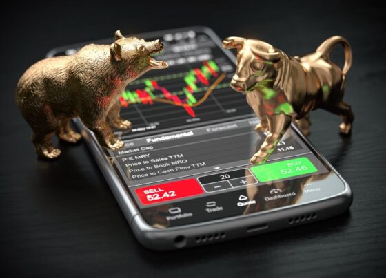 Statues of a bull and bear atop a phone with stock charts.