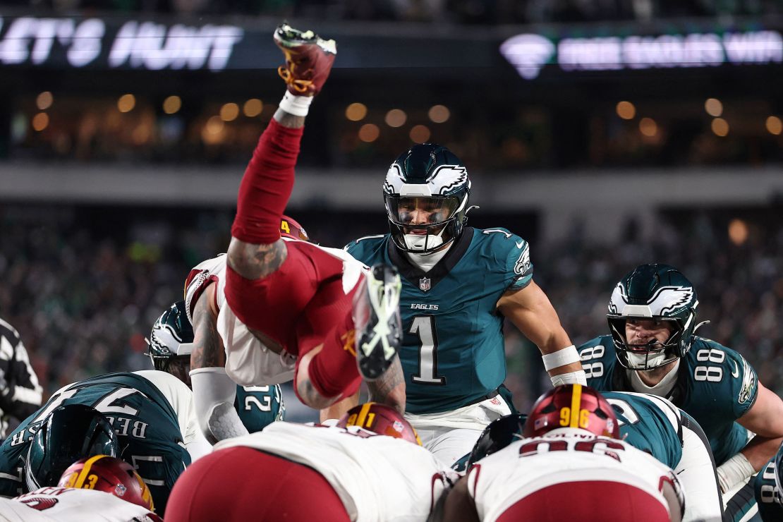 Philadelphia Eagles quarterback Jalen Hurts (No. 1) watches as Washington Commanders linebacker Frankie Luvu leaps over the line.